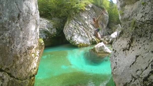 Lassú mozgás: izgatott ember leugrik egy nagy szikláról, és a türkiz Soca folyóba. — Stock videók