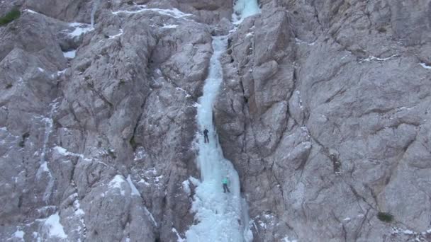 DRONE Vliegen naar een rotsachtige muur als twee ijsklimmers de bevroren waterval beklimmen — Stockvideo