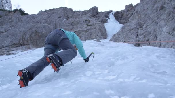 BOTTOM UP: Mujer escalada de hielo se detiene y mira hacia arriba en la hermosa cascada congelada . — Vídeos de Stock