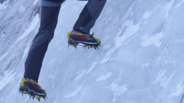 Yaklaşan dağcı donmuş dereye tırmanırken kramponlarını buza sokuyor.