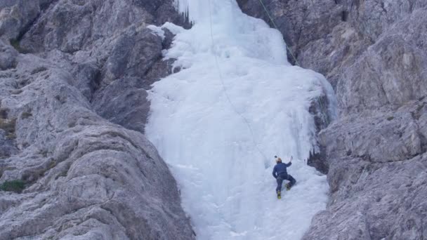 Hombre atlético con crampones y hachas de hielo sube a la hermosa cascada congelada. — Vídeo de stock