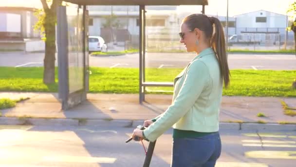 CERRAR: Joven mujer milenaria monta un scooter eléctrico fresco en un día soleado — Vídeo de stock