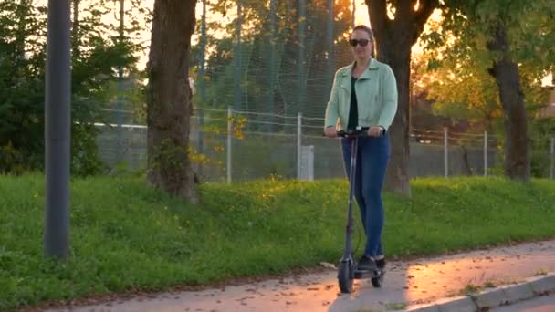 Lykkelig ung kvinne kjører elektrisk scooter en solfylt høstkveld.. – stockvideo