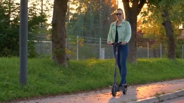 SONNENFLÄCHE: Frau genießt bei Sonnenuntergang eine Rollerfahrt entlang der fallenden Allee. — Stockvideo