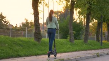 LENS FLARE Kadın banliyöde boş bir kaldırımda elektrikli scooter sürüyor