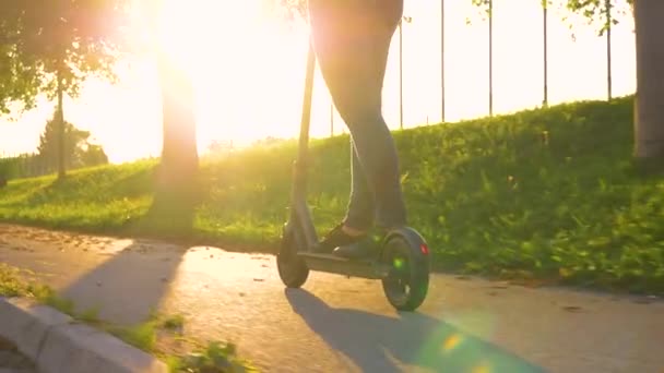 COPY SPACE: Cinematic shot van een meisje in jeans rijden een e-scooter bij zonsondergang. — Stockvideo