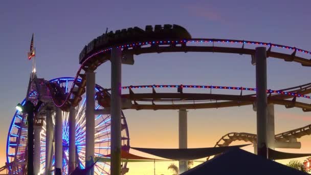 SILHOUETTE: Gouden avondzonnestralen verlichten de achtbaan en het reuzenrad. — Stockvideo