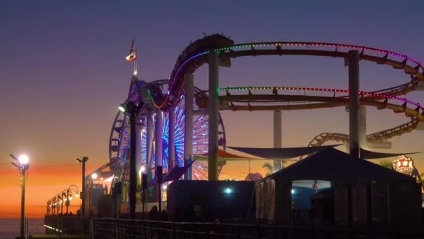 SILHOUETTE: Vista panorâmica do parque de diversões no cais de Santa Monica ao pôr-do-sol. — Vídeo de Stock