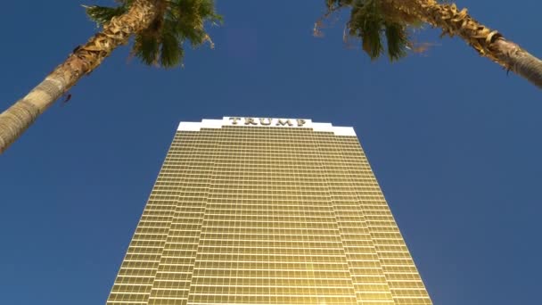 閉じる:緑豊かなヤシの木の上のラスベガスの塔の大規模な金色のトランプホテル. — ストック動画