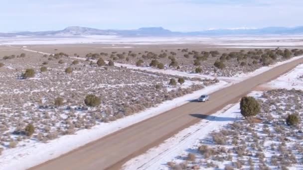 AERIAL: Rodeando un coche mientras atraviesa las llanuras nevadas de Montana. — Vídeo de stock