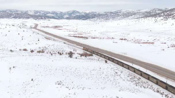 DRONE: Los coches conducen a lo largo de la carretera corriendo por las vías que conducen tren a través del valle. — Vídeo de stock