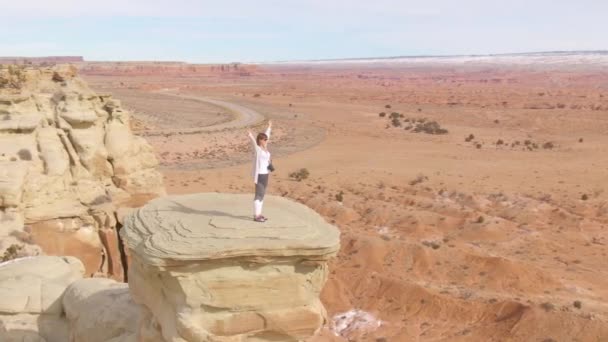 AERIAL: boldog női hegymászó áll a szikla tetején sikeres mászás után. — Stock videók