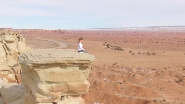 AERIAL: Joven escalador se sienta en el borde de una formación rocosa con vistas al desierto — Vídeo de stock