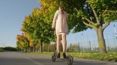 Yüksek topuklu giyen tanınmayan genç bir kadın işe e-scooterla gidiyor..