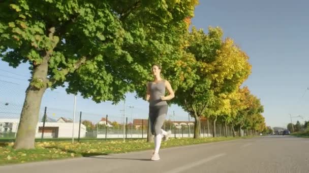 ÂNGULO BAIXO: Mulher sorridente gosta de uma corrida divertida ao longo da passarela colorida do outono . — Vídeo de Stock