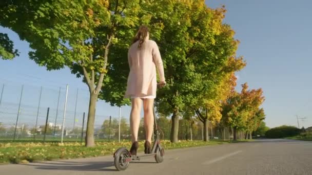 ÁNGULO BAJO: El viajero femenino monta un scooter eléctrico a lo largo de una avenida de color otoño — Vídeo de stock