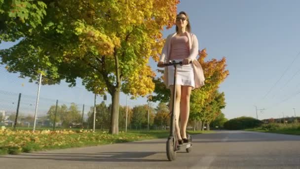ÁNGULO BAJO: Joven mujer viaja a lo largo de una avenida de color otoño en e-scooter . — Vídeos de Stock