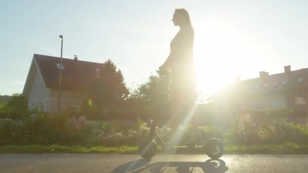 LENS FLARE: Modern tusenårig kvinna pendlar genom förorter på en e-scooter — Stockvideo