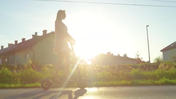 ESPACIO DE COPIA: Mujer joven monta un scooter eléctrico a través de suburbios al atardecer . — Vídeos de Stock