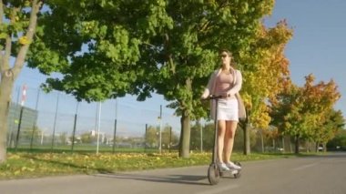 Mutlu kız sonbahar renkli ağaçların yanından geçerken e-scooter kullanıyor..