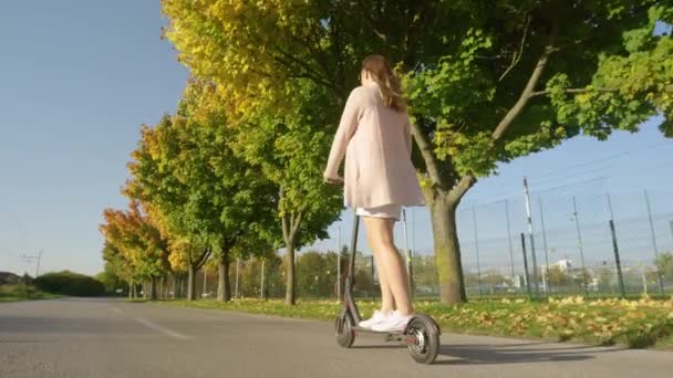 LOW ANGLE: Moderne Frau fährt im Herbst mit Elektroroller durch die Vorstädte — Stockvideo