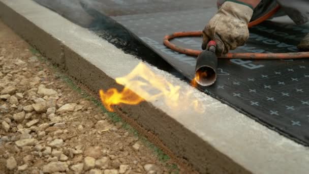 FERMETURE : L'entrepreneur brulant une torche brûle un rouleau de goudron sur la fondation. — Video