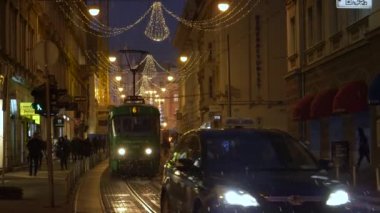 Tramvay, araba ve yayalar Noel zamanı Zagreb 'de bir cadde boyunca ilerliyor.