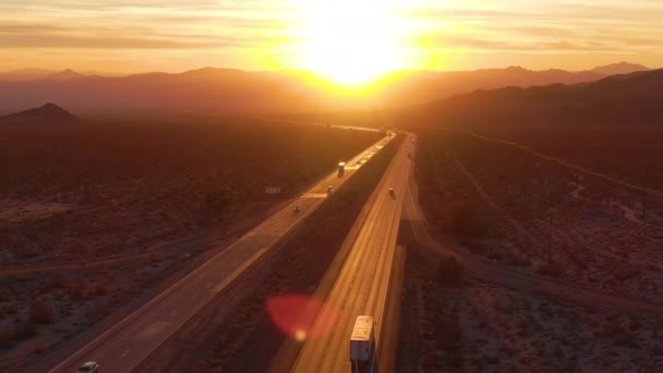 AERIAL: Voando acima de caminhões e carros que atravessam o deserto de Mojave ao pôr do sol . — Vídeo de Stock