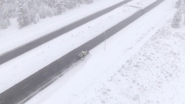 Flyger över en vintrig vintergrön skog när snöplogen rensar den isiga landsvägen. — Stockvideo