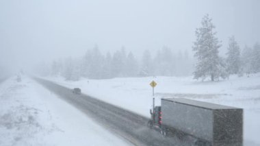Yarı kamyonlar ve arabalar korkunç hava koşullarında karlı bir yolda yol alırlar..