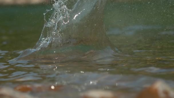 Капли стеклянной воды летят в воздухе после того, как галька падает в реку . — стоковое видео