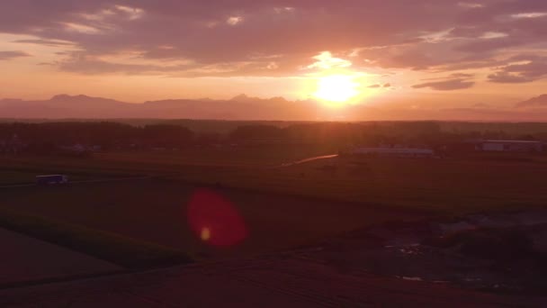 AERIAL: Zachód słońca oświetla krajobraz dla pojazdów jadących wzdłuż malowniczej drogi. — Wideo stockowe