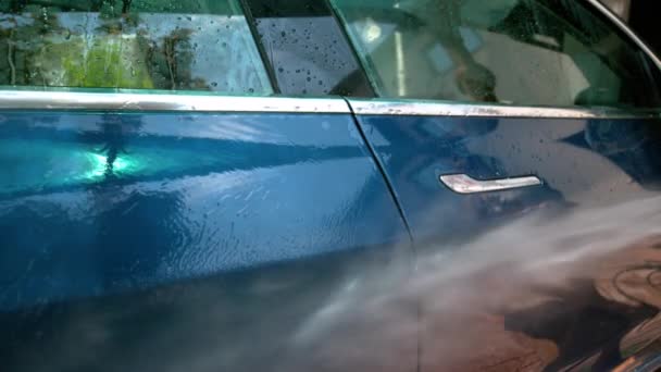 CLOSE UP: Water wordt gespoten over de zijkant van een blauwe auto die wordt gewassen op de oprit. — Stockvideo