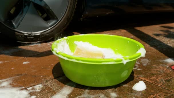 Sluiten omhoog: Persoon wassen van een auto druppels een spons in een emmer vol met zeep water — Stockvideo