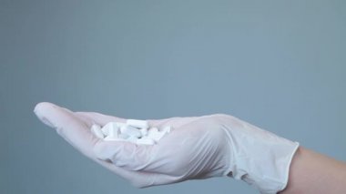 Tıbbi eldivenli kadın beyaz oval haplar alıyor.