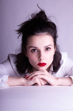 Dudaklarında kırmızı ruj lekesi olan beyaz arka planda beyaz gömlekli güzel bir genç kız.