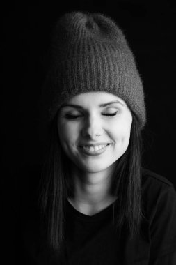 Şapkalı güzel bir genç kız gülümsüyor. Portre stüdyosu, siyah beyaz fotoğraf.