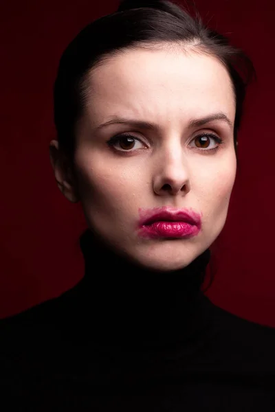 girl in a black turtleneck on a red background with smeared lipstick on her face