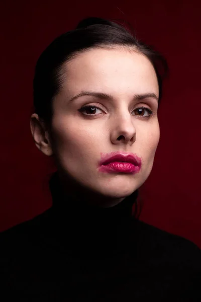 girl in a black turtleneck on a red background with smeared lipstick on her face