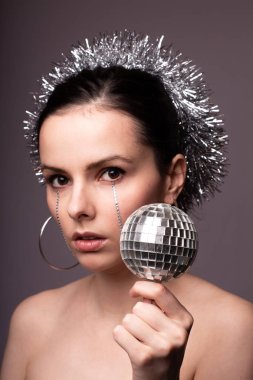 Gümüş süslemelere sarılmış güzel bir kız, elinde sahte elmaslarla elinde bir disko topu.