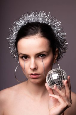 Gümüş süslemelere sarılmış güzel bir kız, elinde sahte elmaslarla elinde bir disko topu.