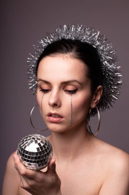 Gümüş süslemelere sarılmış güzel bir kız, elinde sahte elmaslarla elinde bir disko topu.