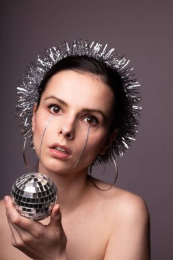 Gümüş süslemelere sarılmış güzel bir kız, elinde sahte elmaslarla elinde bir disko topu.