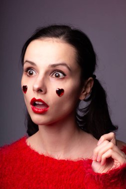 Kırmızı dudaklı ve yüzünde kırmızı bir kalp olan kırmızı kazaklı bir kız.