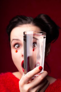 Kırmızılı duygusal kız kırmızı dudaklı ve yüzünde sahte elmaslarla elinde bir bardak tutuyor.