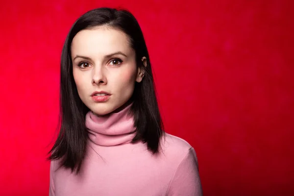 beautiful girl in a pink turtleneck on a red background