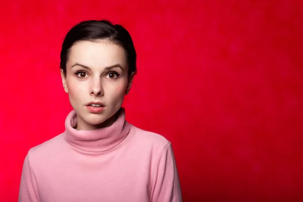 beautiful girl in a pink turtleneck on a red background