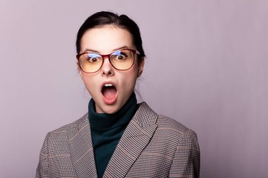 Yeşil balıkçı yakalı kız, ceket, gözlük, gri arka planda portre.