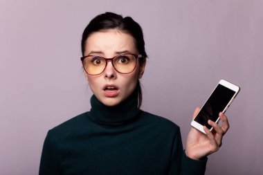 Yeşil balıkçı yaka ve gözlüklü kız telefonla iletişim kuruyor, gri arka planda portre çiziyor.
