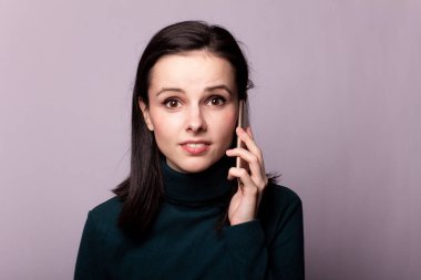 Yeşil balıkçı yakalı bir kız telefonla konuşuyor, gri arka planda bir portre.